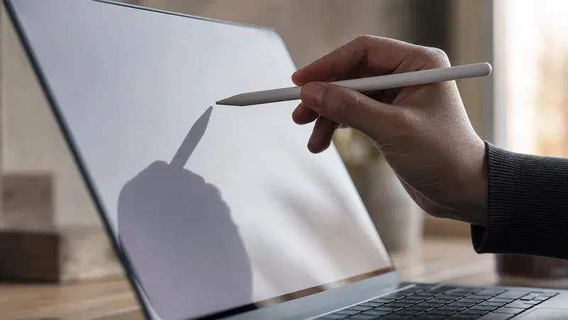 A hand holding a stylus just above a laptop screen, representing annotating directly on what is on display